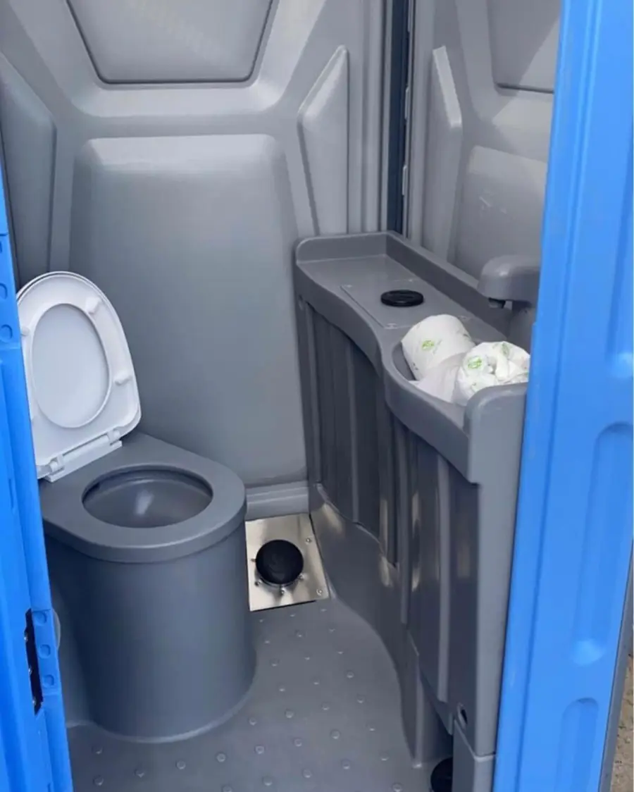 Inside a deluxe flushing porta potty with a toilet, side counter and paper towel holder