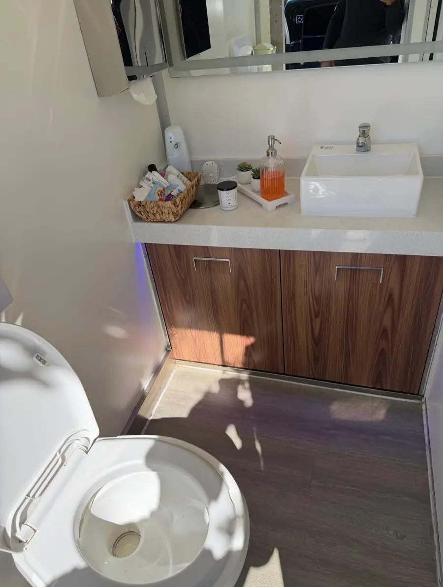 Restroom trailer interior with a white vessel sink on a wood vanity and a toilet beside it