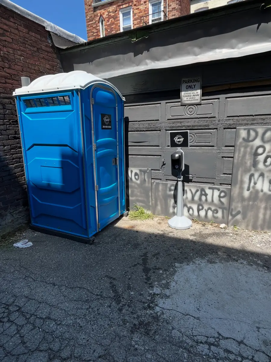 Standard porta potty set on pavement beside a building, out of low icy spots