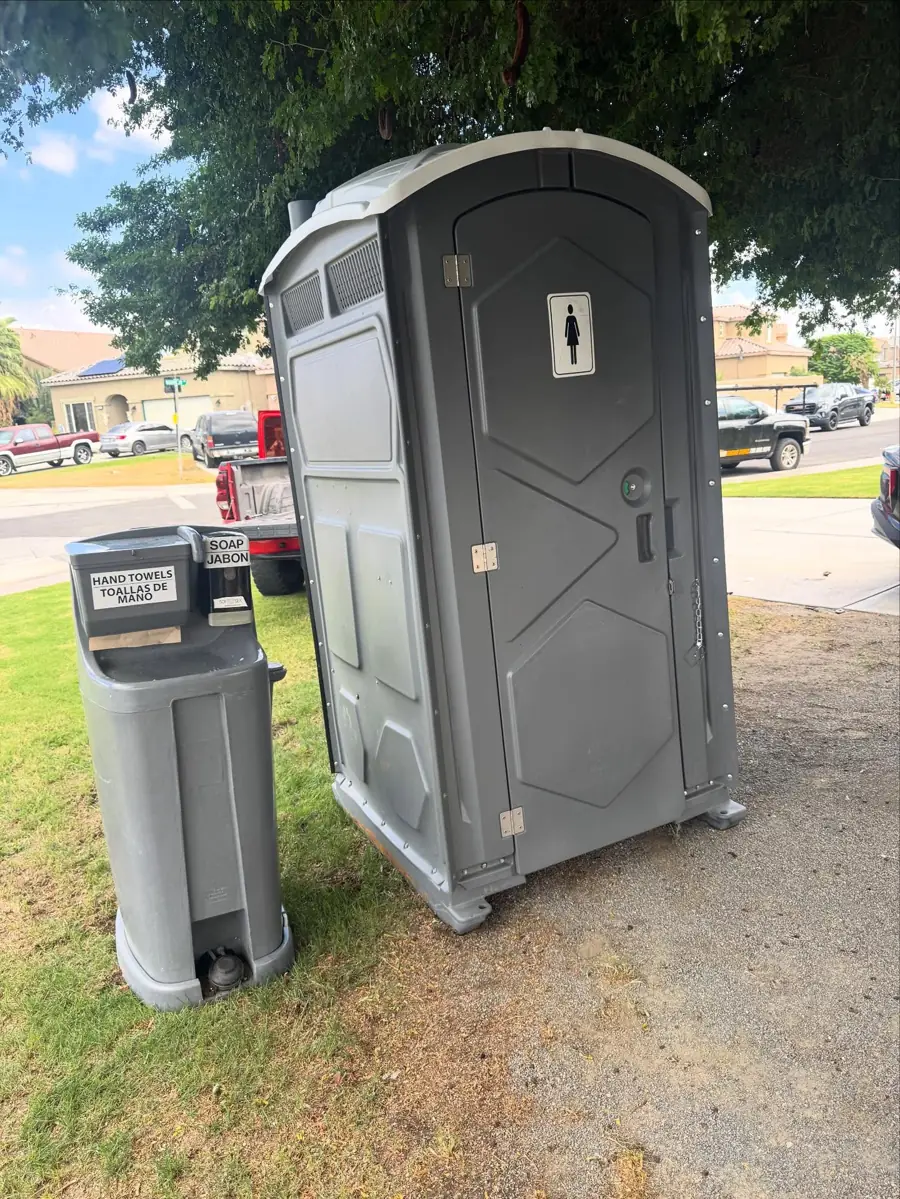 Foot-pump hand washing station standing next to a portable toilet on grass